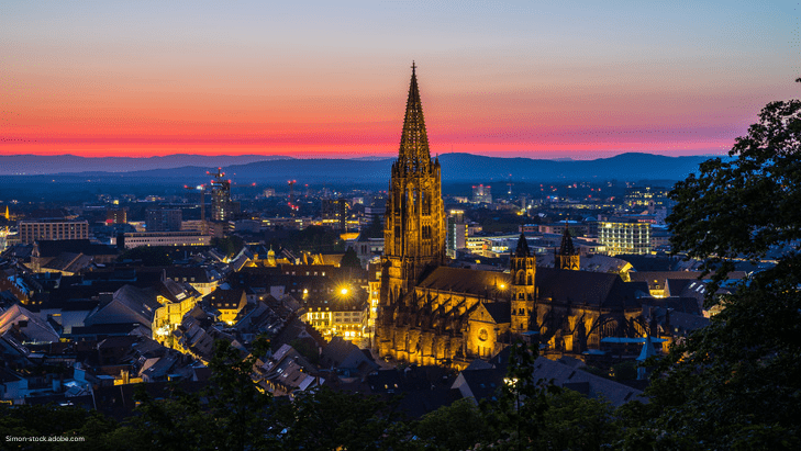 Auf dem Bild ist die Stadt Freiburg und ihr Münster bei Sonnenuntergang zu sehen.